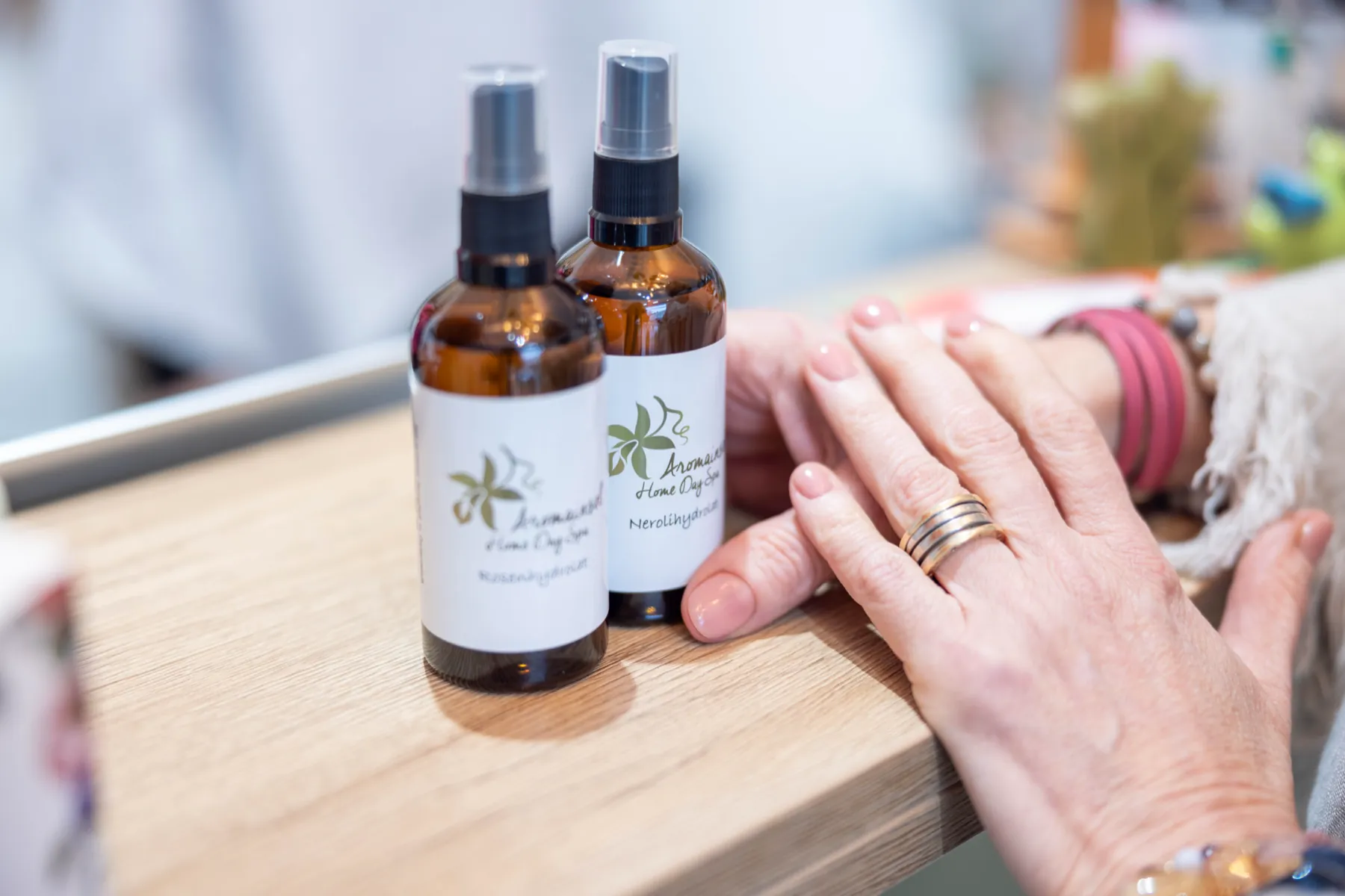 Zwei Aromainsel-Sprays auf einer Holztheke, daneben die Hände einer Kundin