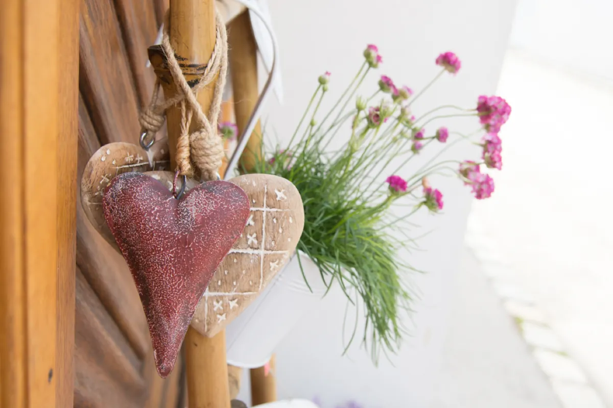 Zwei dekorative Herzen an einer Holzwand, daneben rosa Blumen